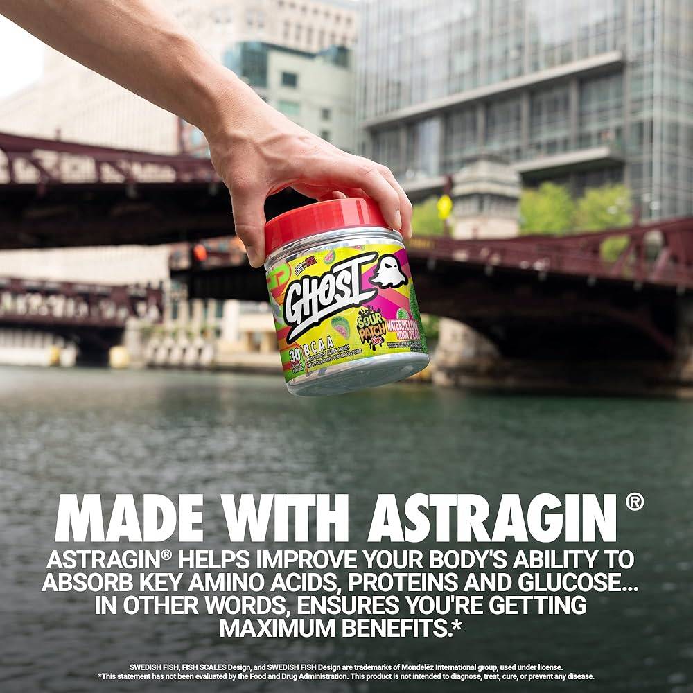 Hand holding GHOST BCAAs Sour Patch Kids Redberry tub near water, highlighting Astragin® benefits for amino acid absorption.