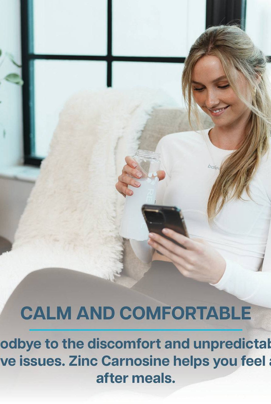 Woman relaxing indoors with a water bottle and phone, promoting Revive Zinc Carnosine for digestive comfort and ease after meals.