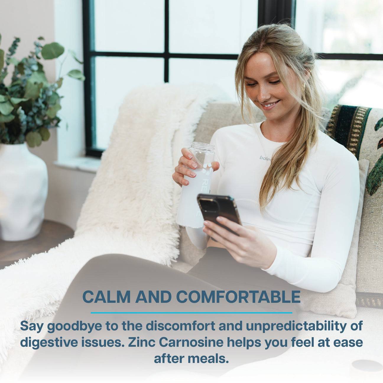 Woman relaxing indoors with a water bottle and phone, promoting Revive Zinc Carnosine for digestive comfort and ease after meals.