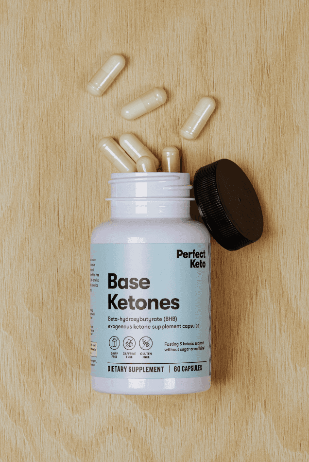 Open bottle of Perfect Keto Base Ketones capsules on wood surface with capsules spilled. Ideal for keto diet and fasting support.