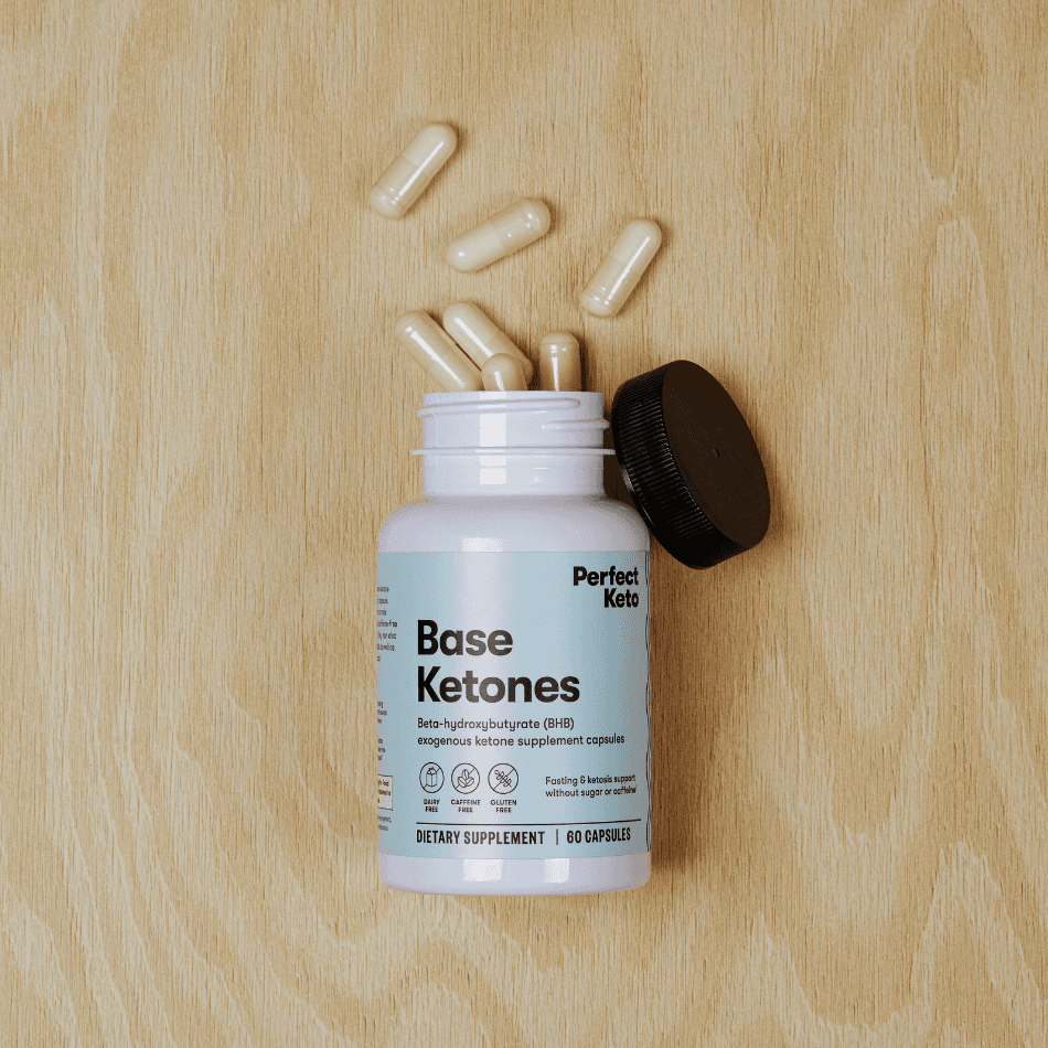 Open bottle of Perfect Keto Base Ketones capsules on wood surface with capsules spilled. Ideal for keto diet and fasting support.