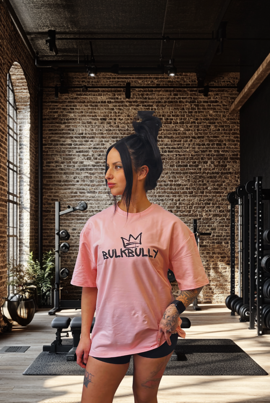 Women's Pink Oversized Tee from BulkBully's G.O.A.L.S Collection, front view worn in a modern gym setting. Features bold BULKBULLY logo print.