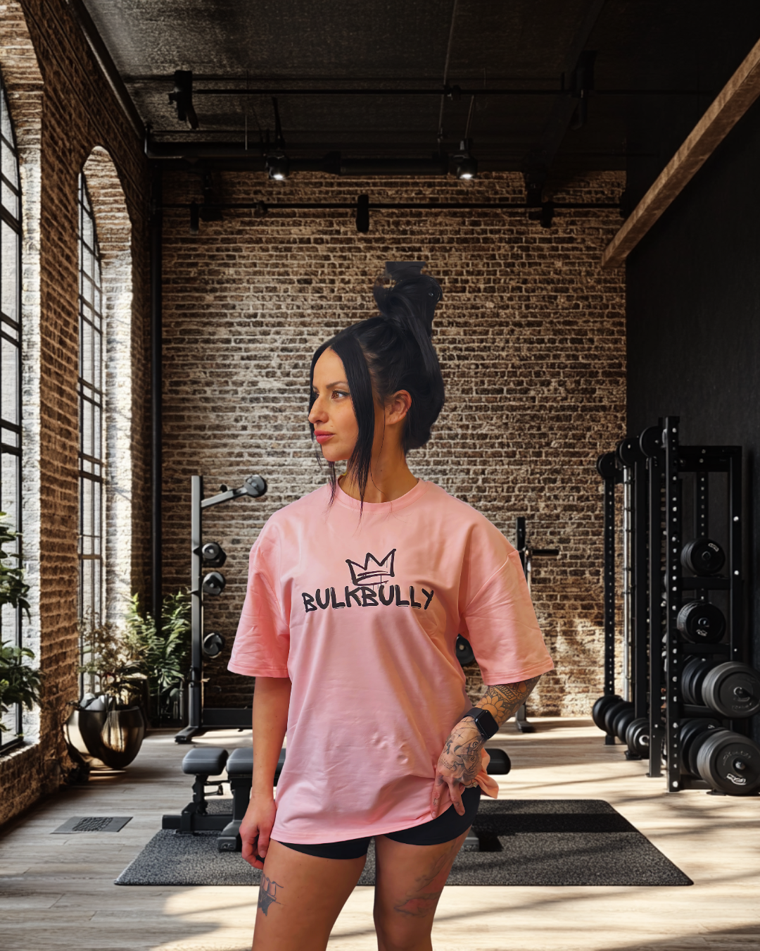 Women's Pink Oversized Tee from BulkBully's G.O.A.L.S Collection, front view worn in a modern gym setting. Features bold BULKBULLY logo print.
