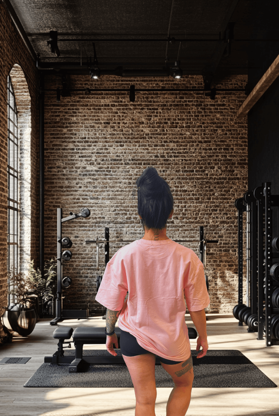 Women's Pink Oversized Tee from BulkBully's G.O.A.L.S Collection, shown from behind in a chic gym environment, highlighting relaxed fit and length.