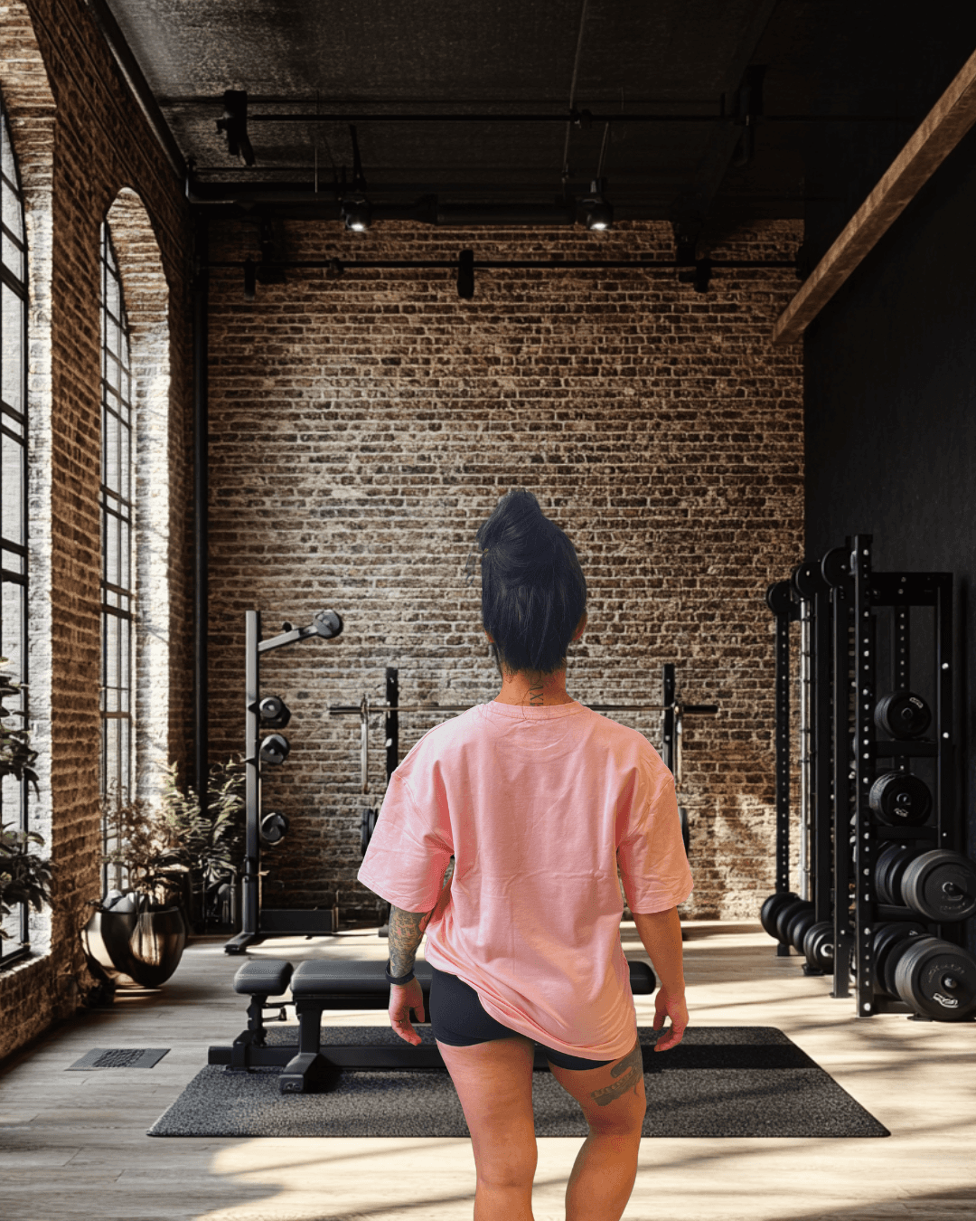 Women's Pink Oversized Tee from BulkBully's G.O.A.L.S Collection, shown from behind in a chic gym environment, highlighting relaxed fit and length.